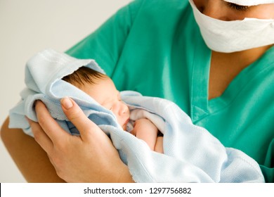 Maternity nurse wearing scrubs holding newborn baby wrapped in blanket