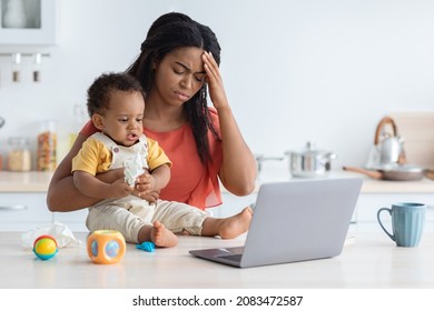 Maternity Stress. Young Black Mother Having Headache While Babysitting Her Infant Child, Tired African American Woman Suffering Acute Migraine While Spending Time With Toddler Baby In Kitchen At Home