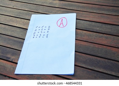 Math exercises on a sheet of notebook and note on it on a wooden table