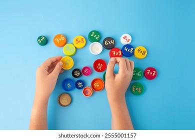 Math learning game with child hands sorting colorful caps with multiplication problems on blue surface, creative educational tool, multiplication table activity, fun math training, kids school math