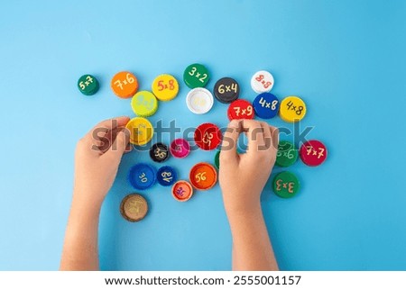 Math learning game with child hands sorting colorful caps with multiplication problems on blue surface, creative educational tool, multiplication table activity, fun math training, kids school math