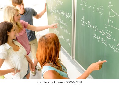 Math lesson student write on green chalkboard with classmates pointing