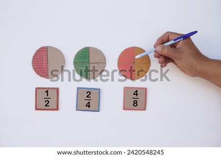 Math teaching materials about fraction. Hand hold pen to point at circle paper to show parts of color separation. Concept, education. DIY craft as teaching aid in Math subject.                        