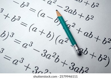 Mathematical equations filled with variables lie under a green pencil.