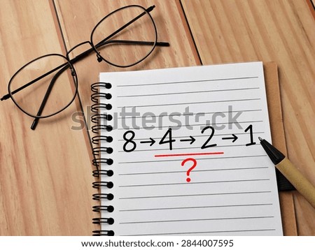 Mathematical Sequence and Logic Puzzle with Division Pattern on Spiral Notebook, Glasses and Wooden Desk Background for Education and Problem Solving. 