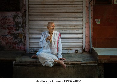 MATHURA, INDIA - OCTOBER 11, 2019: Candid Portrait Of Older Man Sitting Cross-legged Looking Thoughtful And Drinking Tea In Street Scene On October 11, 2019 In Mathura, Uttar Pradesh, India.