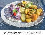 Matjes or soused herring in apple cream sauce with onions, fried potatoes, pickles and salad on a plate in an outdoor restaurant on a sunny summer day, selected focus, narrow depth of field