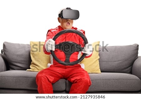 Matrue man in a car racing suit wearing vr headset and holding a steering wheel seated on a sofa isolated on white background