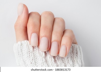 Matt nude nails close up o the light background. Winter manicure, woman hand in the warm sweater.