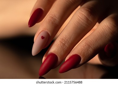 Matte red nails with small red heart on a beige colour nail. Saint Valentine's nail design. 