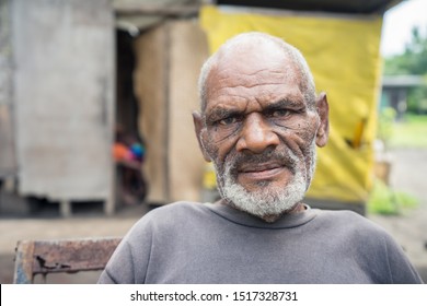 Matupit, East New Britain / Papua New Guinea - July 6, 2019: Portrait Of Elder Of The Tolai Indigenous People With White Beard And Serious Look Sitting In Front Of His House