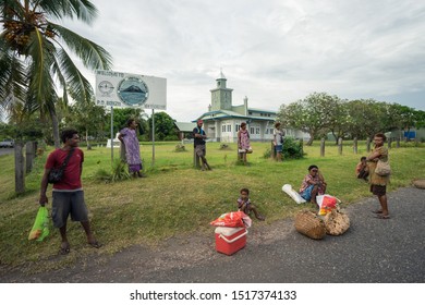 Matupit, East New Britain / Papua New Guinea - July 6, 2019: Tolai Indigenous People Waiting For Transportation Sitting Near Village Church Next To The Road And On The Grass