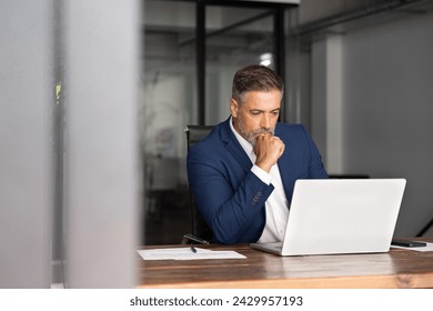 Mature 40s focused businessman, executive director working using laptop, doing data base online research sitting at office. Successful business man, leader, ceo manager, trader trading crypto currency - Powered by Shutterstock