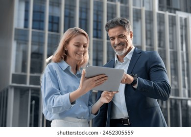 Mature 40s years old man, young adult woman walking, discussing project on digital pc tablet computer. Successful middle aged latin hispanic businessman, businesswoman work together on business plan - Powered by Shutterstock