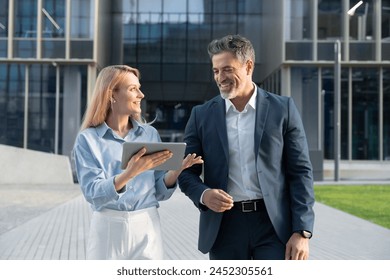 Mature 40s years old man, young adult woman walking, discussing project on digital pc tablet computer. Successful middle aged latin hispanic businessman, businesswoman work together on business plan - Powered by Shutterstock