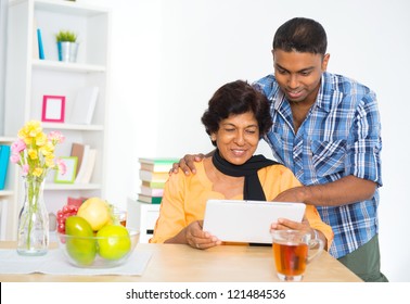 Mature 50s Indian Woman And Son Using Digital Computer Tablet At Home