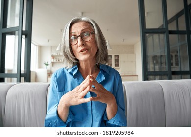 Mature 60s old woman online teacher, remote tutor, distance coach therapist businesswoman talking to web cam virtual counseling conference video calling at home office. Headshot portrait. Webcam view.