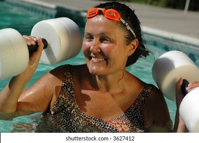 Mature active woman working out in the pool with styrofoam dumbbells - Powered by Shutterstock