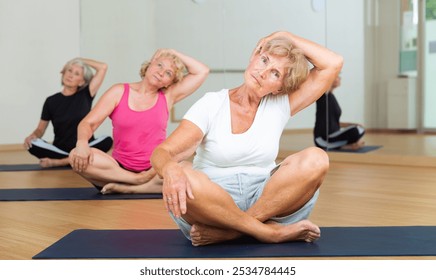 Mature active women practicing yoga in a fitness studio perform an exercise in the lotus position, holding their head with ..their hand - Powered by Shutterstock