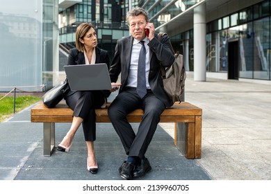 Mature Adult Business Woman Discussing Work With Senior Male Colleague, Two Business Associates Working Together Outside And Talking Over A Business Report, Entrepreneur Using Laptop And Smartphone