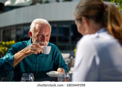 Mature adult businessman drinking coffee in outdoor cafe and looking into pretty young woman - Powered by Shutterstock