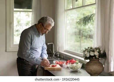 Mature Adult Man Cooking Dinner At Home, Cutting Fresh Vegetables For Salad In Kitchen. Old Senior Pensioner Keeping Healthy Diet And Lifestyle, Taking Care About Nutrition, Eating Raw Organic Food