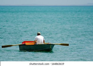 Mature adult man rowing a small wooden rowboat dinghy over calm sea ocean water. Human freedom to travel concept. Real people. Copy space - Powered by Shutterstock