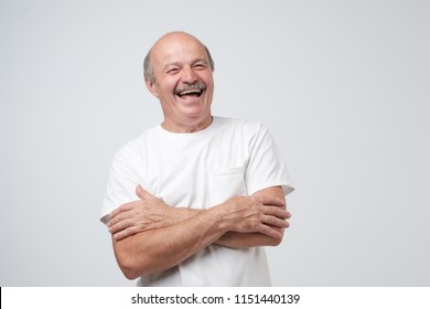 Mature Adult Man In White Tshirt With Moustache Laughing Looking At The Camera Over White Background. Some Jokes Are Old But Gold. Positive Emotion Concept