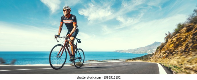 Mature Adult on a racing bike climbing the hill at mediterranean sea landscape coastal road - Powered by Shutterstock