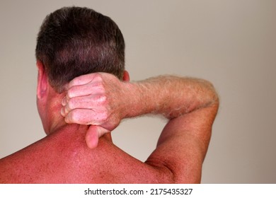 Mature adult white male seen from rear view massaging the back of his neck under his brown hair. Rear view of a naked caucasian man massaging his painful neck to help to relax his muscles close-up