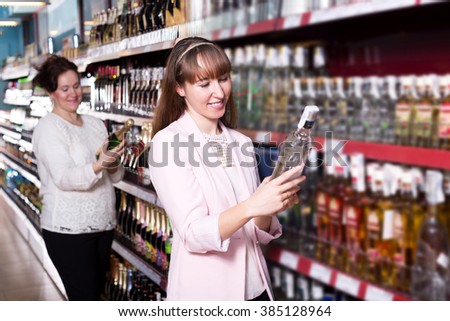 Mature and adult women selecting bottle of vodka in supermarket and smiling