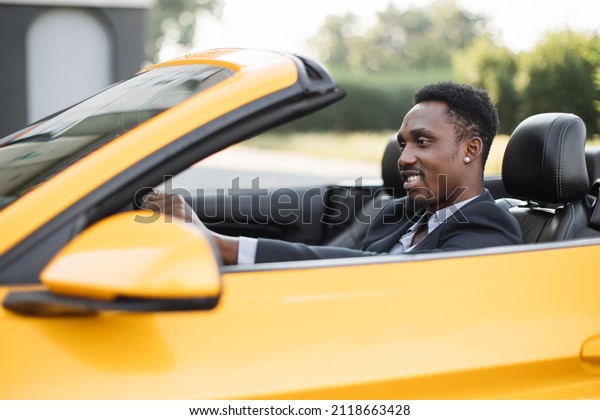 Mature African\
American business man sitting in the luxury sport vehicle and\
smiling looking aside. Portrait of an handsome smiling African man\
driving his car with formal\
suit