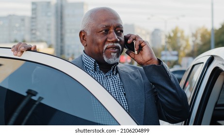 Mature African American Businessman Standing Near Car Outdoors In Parking Lot Speaks On Mobile Phone Elderly Friendly Man Communicates On Telephone Answers Call Using Smartphone Talking By Cellphone