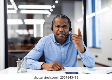 Mature african american businessman wearing headset expresses frustration in office. Engaged in intense phone call, pointing finger during a virtual meeting. Concept of leadership, communication. - Powered by Shutterstock