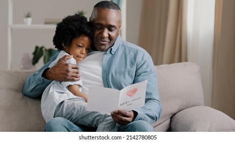 Mature african american man with cute kid girl hugging sitting in room on sofa father reads greeting card loving daughter made gift with own hands for birthday or father's day dad happy cuddling baby - Powered by Shutterstock