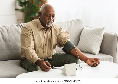 Mature African American Man Measuring Arterial Blood Pressure With Sphygmomanometer Medical Device Sitting On Couch Indoors. High Blood-Pressure, Hypertension Health Problem Concept