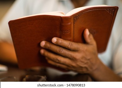 Mature African American man praying and reading the Bible.
