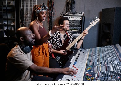 Mature African American Music Producer, Young Female Singer And Male Guitarist Working On Song In Recording Studio