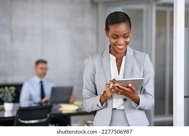 Mature african businesswoman using digital tablet while standing in modern office. Black confident business woman working on digital tablet in meeting room with copy space. Happy successful woman.
