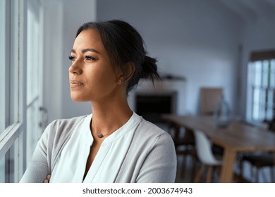 Mature african woman looking outside window with uncertainty. Thoughtful mid adult woman looking away through the window while thinking about her future business after pandemic. Doubtful lady at home.