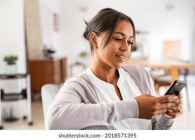 Mature African Woman Sitting On Couch At Home Using Smartphone. Black Woman Relaxing On The Sofa While Messaging With A Cellphone At Home. Happy Mature Indian Woman Typing On Mobile Phone.