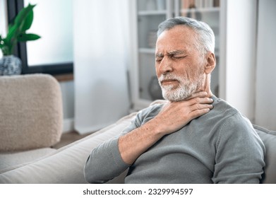 Mature aged man suffering from strong throat sore or angina. Concept of health problems, losing of voice, pain and itching. Elderly person feeling discomfort and difficulty to swallow.