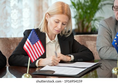 Mature American delegate in formalwear signing contract of business partnership with foreign partner while sitting by table in boardroom - Powered by Shutterstock