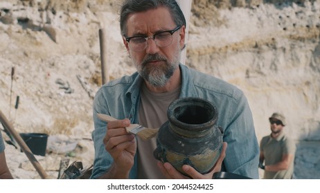 Mature archaeologist discussing antique vessel with colleague