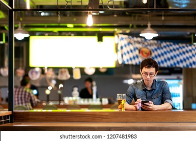 Mature asian chinese man with tired and thoughful face sitting at counter bar, pub or restaurant drinking beer looking at smartphone waiting for friends. Rest in leisure time on Friday night concept. - Powered by Shutterstock