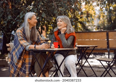 Mature Asian lady with positive grey haired friend spend time together sitting at small table in street cafe on nice autumn day - Powered by Shutterstock