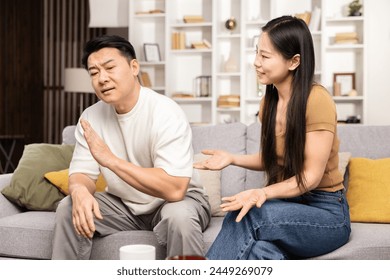 Mature Asian Man Gesturing Stop During Argument, Young Asian Woman Explaining, Couple Dispute, Relationship Problems, Emotional Stress, Indoor Living Room, Conflict Resolution - Powered by Shutterstock