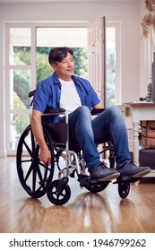 Mature Asian Man In Wheelchair Pushing Himself Along Hallway At Home