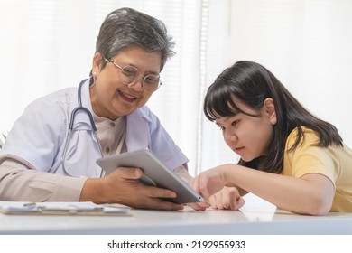 Mature Asian Physician Psychiatrist, General Woman Doctor Consulting Concerned With Child Patient Using Tablet Explaining Diagnosis, Appointment At Clinic, Hospital. Health Care, Check Up Medical.