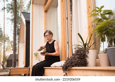 Mature Asian Woman In Black Dress Sitting On Terrace Of Suburb House Using Singing Tibetian Bowl For Meditation